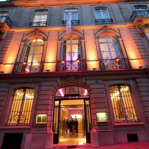Image illustrative représentant la façade d'un immeuble haussmannien, de nuit, éclairé, à Paris