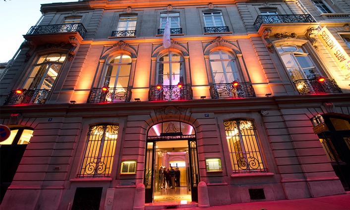 Image illustrative représentant la façade d'un immeuble haussmannien, de nuit, éclairé, à Paris